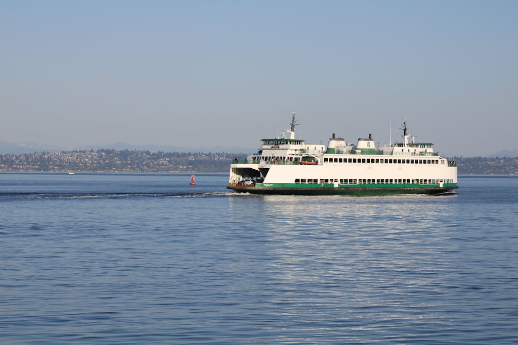 A ferry sails across calm waters near Port Orchard, WA, with scenic city views in the background.